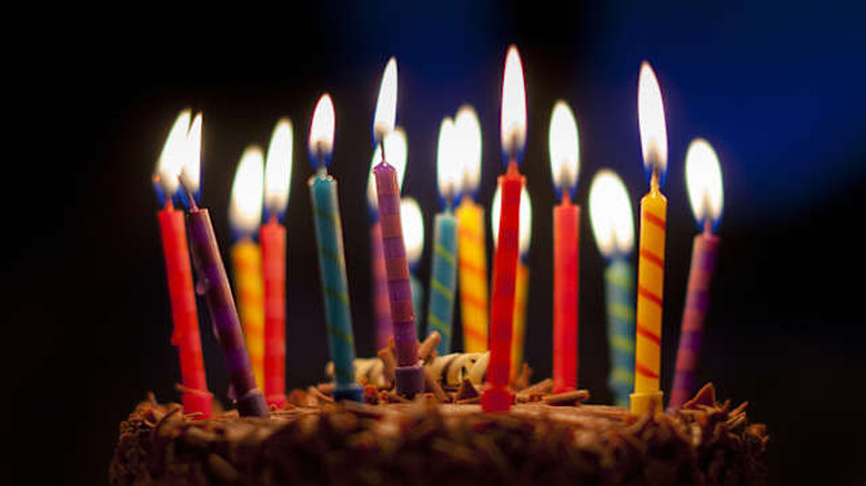 Colourful candles standing on top of a chocolate birthday cake. The candles are lit up against a dark blue background.