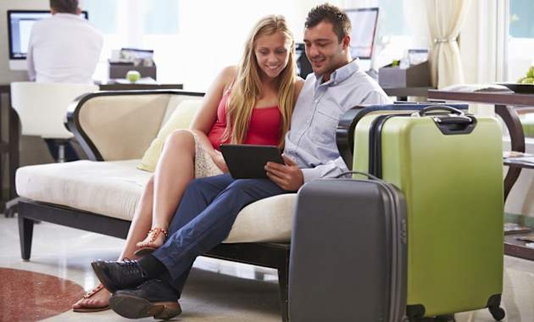 Couple Sitting In Hotel Lobby Looking At Digital Tablet Smiling