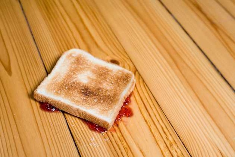 Slice of toast with strawberry jam turned upside down on floor