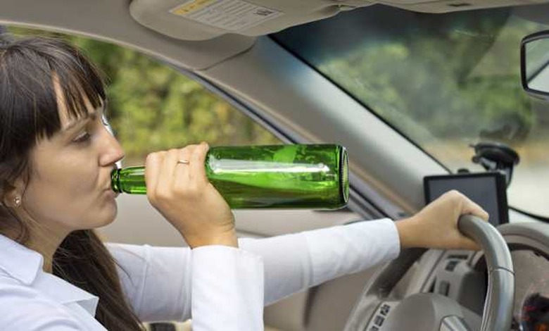 Drunk female driver in her car driving along the road gulping booze directly from the bottle