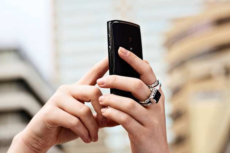 A woman's hands with multiple rings busy texting on a cell phone outside a building raises her hands high, probably trying to ra