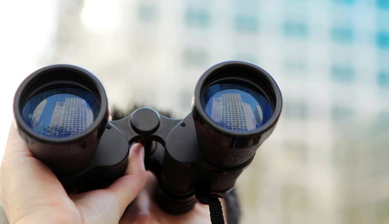 Businessman searching office buildings with binoculars.