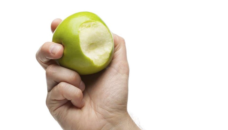 Hand holding green apple with bite missing isolated on a white background