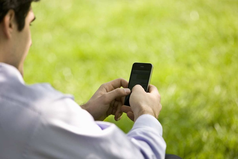 A businessman sitting on the grass, using his mobile phone