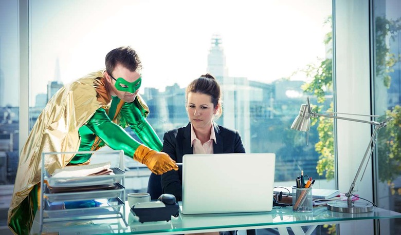 Superhero helping businesswoman working at office desk