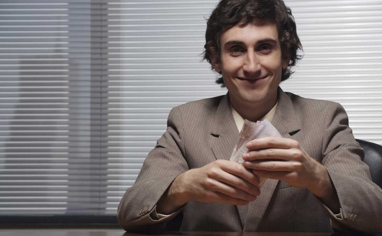 Businessman sitting at desk, holding bank notes, smiling, portrait