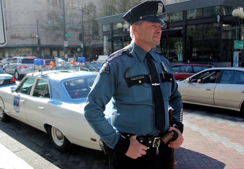 In this image taken Tuesday, April 23, 2013, Seattle police officer Jim Ritter stands behind a 1970 Plymouth Satellite he drives while on patrol in Seattle's Westlake Park. Ritter uses the vintage car as his everyday car and for community outreach for the Seattle Police Department. (AP Photo/Manuel Valdes)