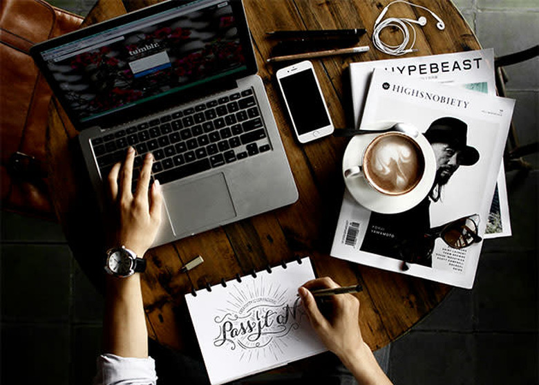 Man in a coffee shop sat at a table working on his laptop