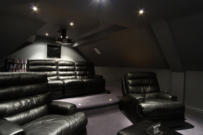A sleek gaming den with a projector, leather sofa and recliner chairs and floor lighting