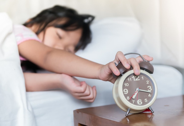 cute girl reaching out for alarm clock
