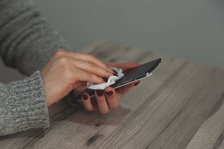The woman cleans the cell phone with a napkin