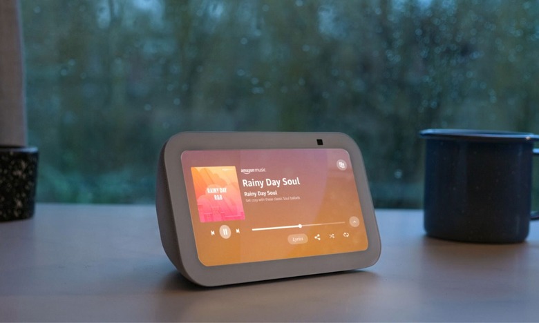 Amazon's Echo Show 5 smart display rests on a tablet in front of a rainy window.