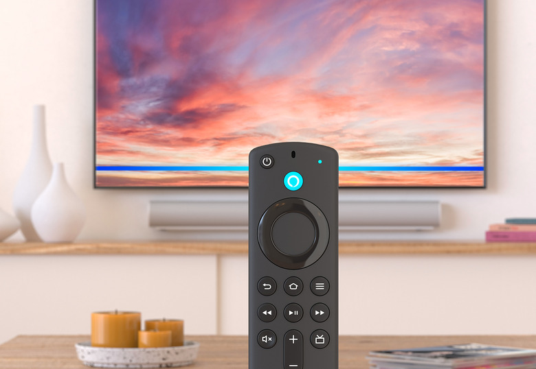 An image of a Fire TV stick standing in front of a TV. There are candles and tasteful vase. 