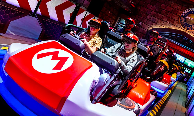 Smiling park visitors sit inside cars at the Universal Studios ‘Mario Kart’ ride. The car has a Mario ‘M’ logo on it.