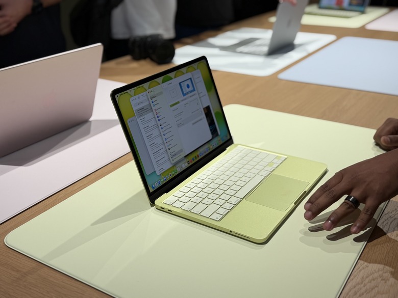The yellow MacBook Neo on a display table with a hand near it.