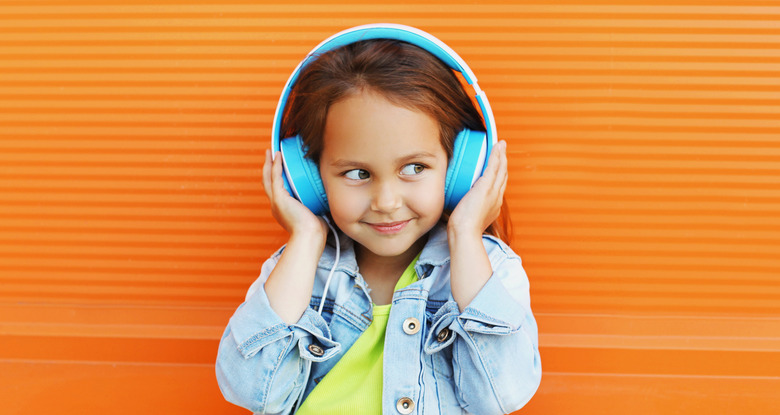Portrait of happy smiling child in headphones listening to music on city street over orange wall background