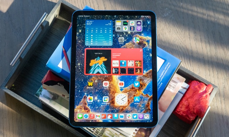 The 2022 iPad (displaying its Home Screen) lying on top of a stack of books. Dramatic lighting from a partially opened window.