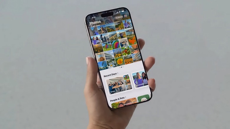 A hand (out of frame from the wrist on) holding an iPhone with the Photos app open. Gray background.