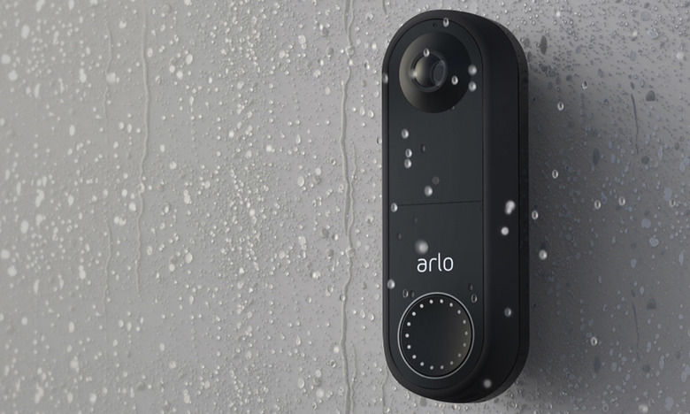 Arlo's video doorbell on a gray wall with raindrops on both the wall and the doorbell. 