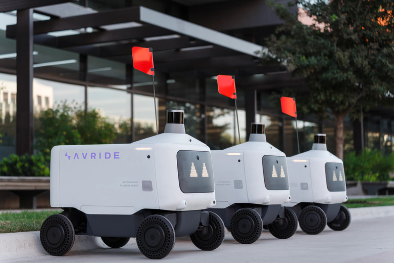 Three Avride autonomous delivery vehicles parked in a line. They have red flags.