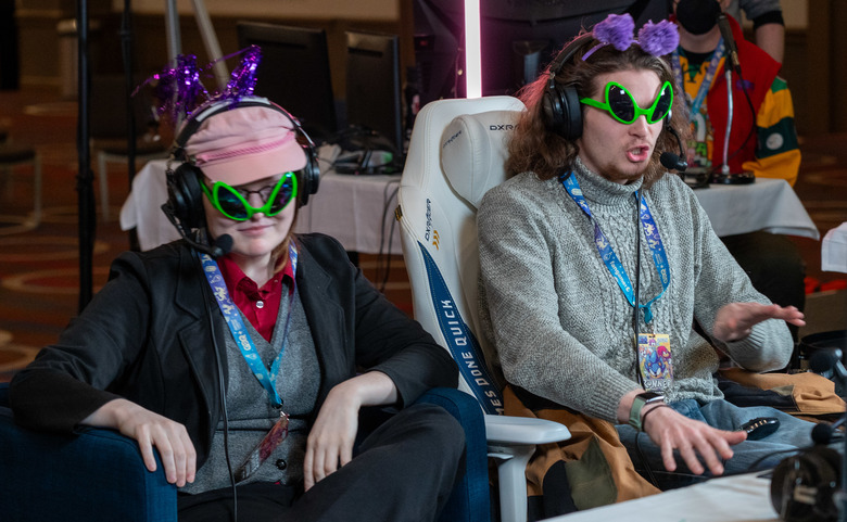 Two people sit in funny headwear and sunglasses watching a speedrun in a conference room at Awesome Games Done Quick 2024