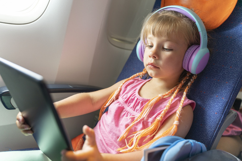Caucasian girl with headphones watching and listening in flight entertainment on board an airplane