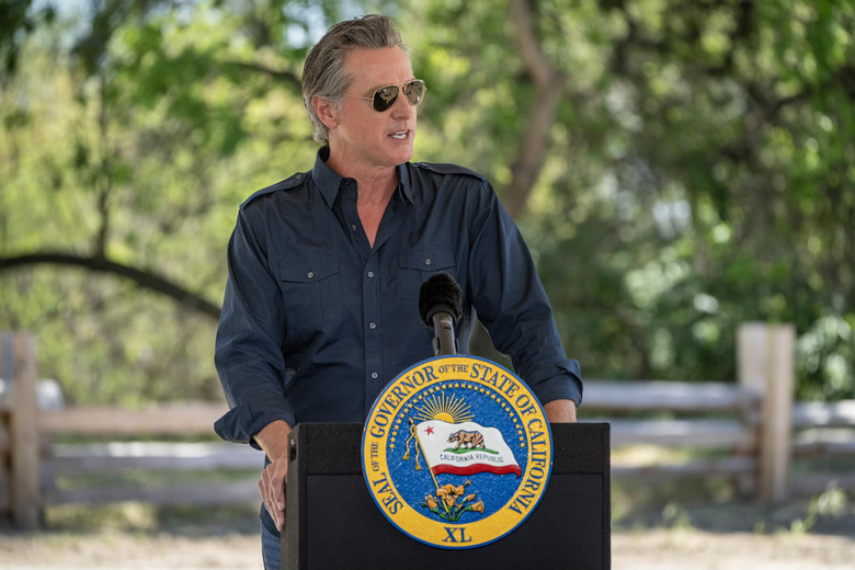 A man wearing a blue dress shirt and sunglasses standing behind a podium 