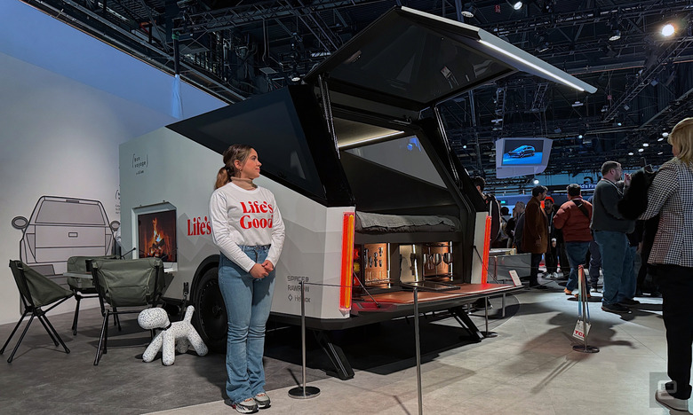 A woman standing next to a high-tech concept trailer from LG at CES 2024. There are camping chairs to the side of the trailer.