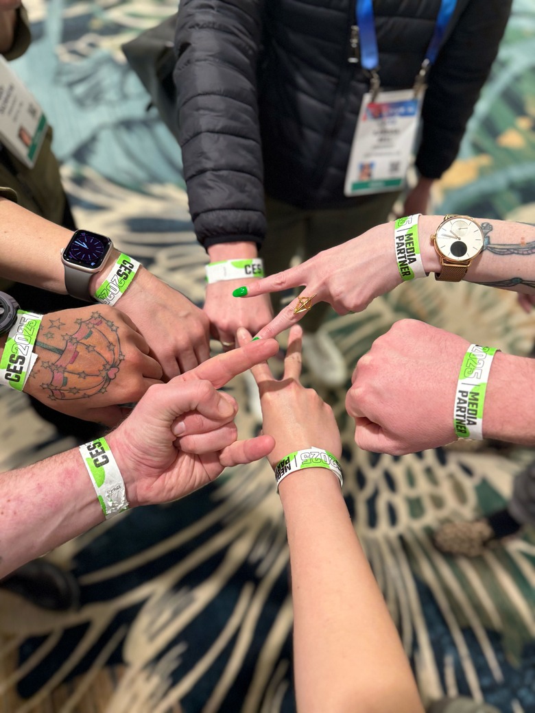 Seven hands in a circle, each with a green-and-white band on it saying CES 2025 media partner.