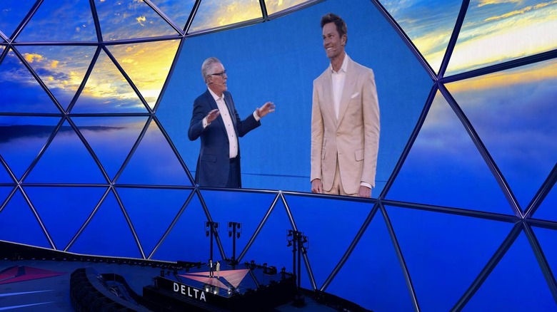 Tom Brady standing next to Delta CEO Ed Bastian, who is looking up at the former athlete with his hands up as if in the middle of raising the roof.