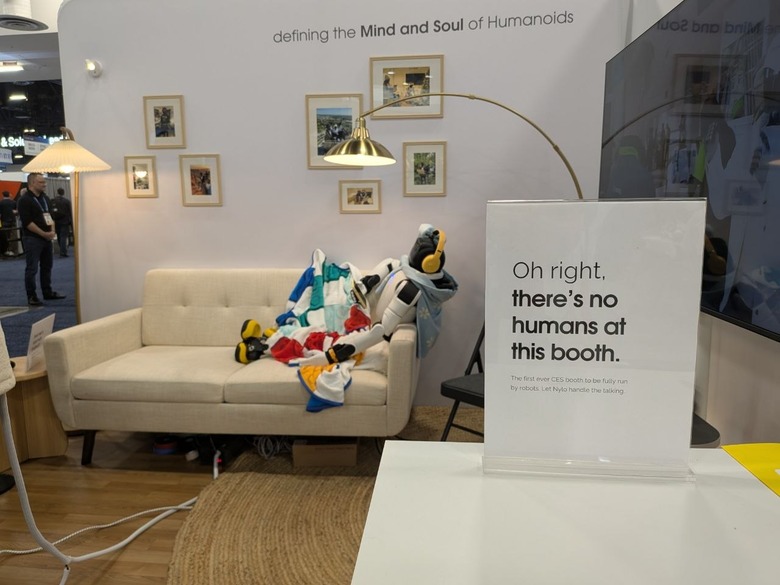 A robot wearing over-ear headphones, draped in a blanket and chilling on a couch at CES 2026