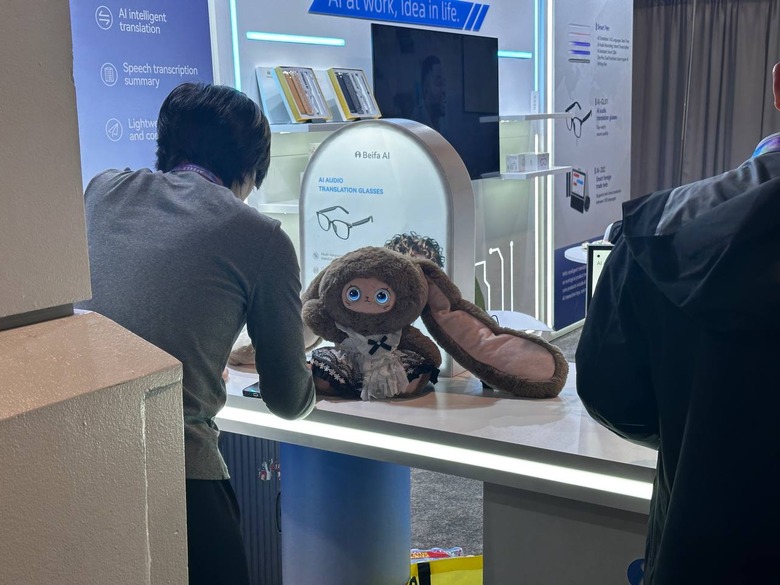 A doll or robot resembling a Labubu with a giant ear sits on a table at a booth at CES 2026