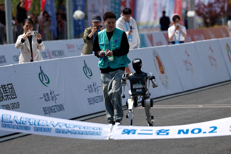 An engineer runs with the humanoid robot Noetix N2 as it runs towards the finish line at second place in the E-Town Humanoid Robot Half Marathon in Beijing, China, April 19, 2025. REUTERS/Tingshu Wang