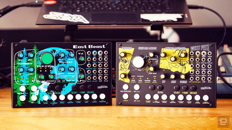 The Cre8Audio East Beast & West Pest synths seen standing on end facing the camera with a raised laptop and studio setup in the background.
