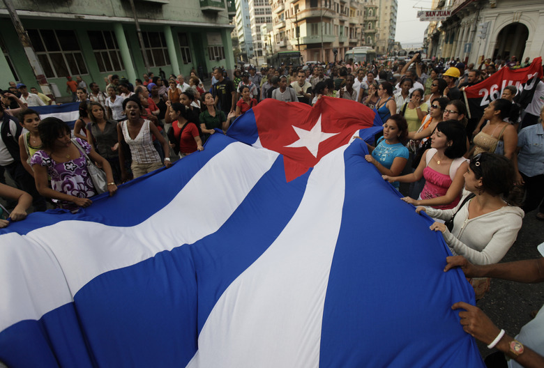 Pro-government youth carry a Cuban flag in front of the Ladies in White, a group made up of family members of imprisoned dissidents, during a protest march in Havana March 25, 2010.  REUTERS/Desmond Boylan (CUBA - Tags: POLITICS CIVIL UNREST)