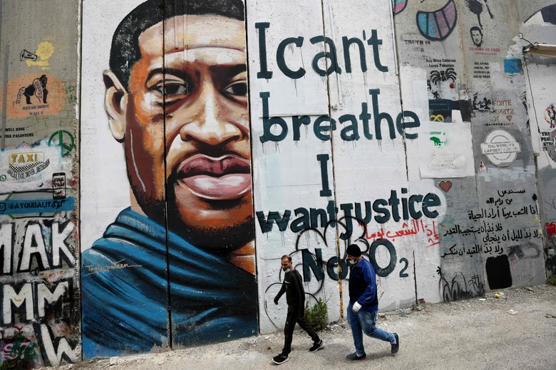 People walk past a mural showing the face of George Floyd, an unarmed handcuffed black man who died after a white policeman knelt on his neck during an arrest in the US, painted on a section of Israel's controversial separation barrier in the city of Bethlehem in the occupied West Bank on March 31, 2021. - The teenager who took the viral video of George Floyd's death said on March 30, at the trial of the white police officer charged with killing the 46-year-old Black man that she knew at the time 