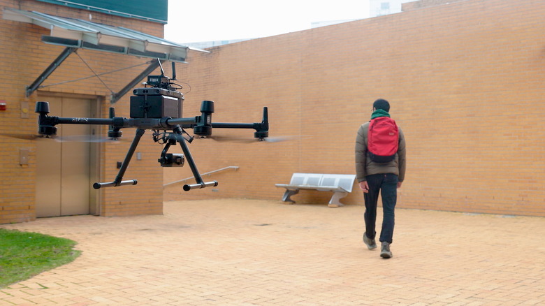 A drone follows a person wearing a backpack.