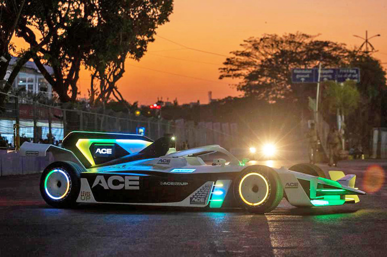 A modified Formula E Gen2 car with glowing accents in yellow, blue and green is seen on a street at dusk with the orange glow of the setting sun providing a warm setting.