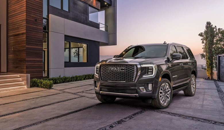 A 2023 GMC Yukon Denali Ultimate is parked out front of a fancy modern home at dusk.