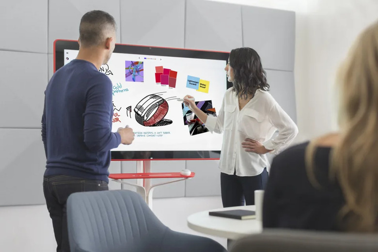 Two people standing in front of a digital whiteboard.