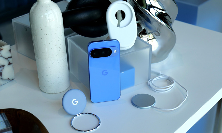 A blue Pixel 10 on a table surrounded by Pixelsnap accessories and ornaments.
