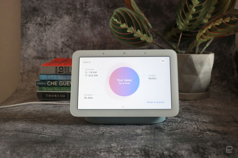 A head-on view of the Google Pixel Tablet resting on its magnetic speaker stand with a plant and small stack of books in the background.