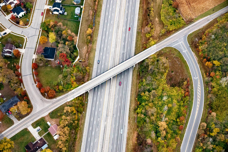 Aerial View; Interstate Highway 75 between Dayton and Cincinnati  features an eight lane highway with a state route bridge overpass.  There is also a Y shaped intersection. The rural scene is in early Autumn.