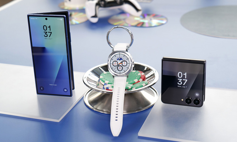 A showcase of three devices. From left to right, a Galaxy Z Fold 7 standing half folded with its external display facing out; a Galaxy Watch 8 Classic hung on a candy holder and a Galaxy Z Flip 7 slightly unfolded and propped up on its camera edge.