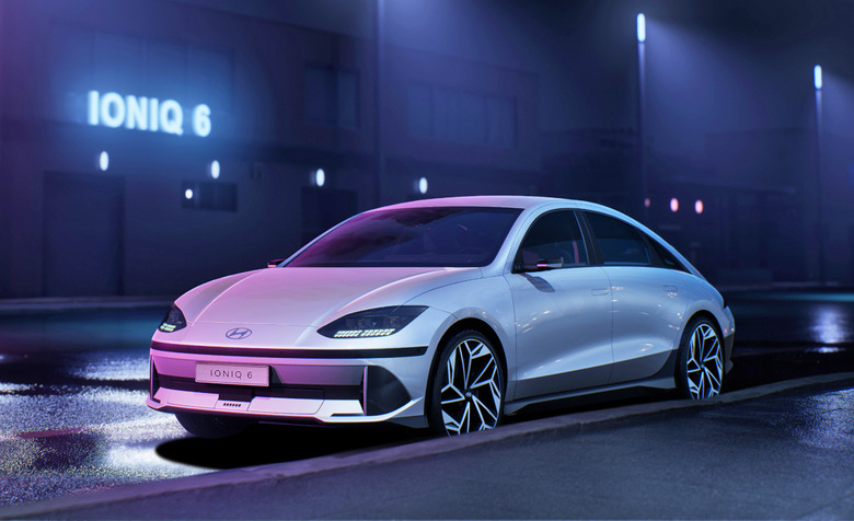 The Hyundai Ioniq 6 parked on a dark wet street lit only by bluish and purple streetlights and a single neon sign with the word Ioniq 6.