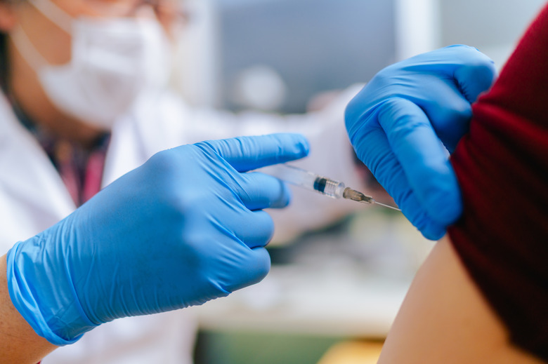 A woman is getting vaccinated by a senior adult doctor in his doctor`s office.