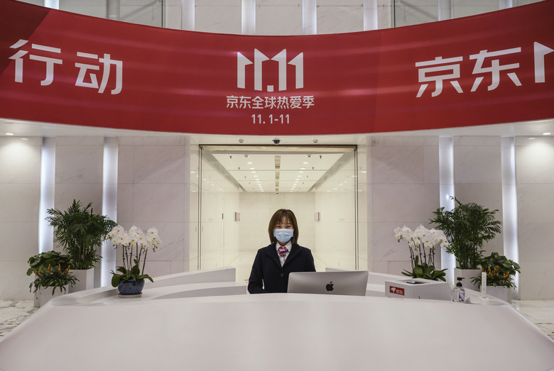 BEIJING, CHINA - NOVEMBER 11: A receptionist from Chinese e-commerce giant JD.com poses from her desk under the Singles Day banner in the lobby at the company's headquarters during an organized tour on November 11, 2020 in Beijing, China. The online shopping blitz, known as Singles Day or Double 11, is the world's largest retail event and comes as Chinese consumers are emerging from the COVID-19 pandemic. The revival of consumer consumption is expected to boost China's economy, which is already showing signs of post-pandemic recovery and providing a bright spot for global brands and retailers. Singles Day sales for China's biggest e-commerce giants like JD.com are on pace to break previous records, pulling in $56 billion U.S. in the first 30 minutes, when combined with three days of pre-event sales. (Photo by Kevin Frayer/Getty Images)