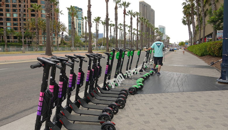 A row of new electric dockless scooters from Lyft is parked by the side of a road in downtown San Diego, ready to be rented. Lyft is one of the latest companies to join the dockless market. In the background, there are also scooters from Limebike.