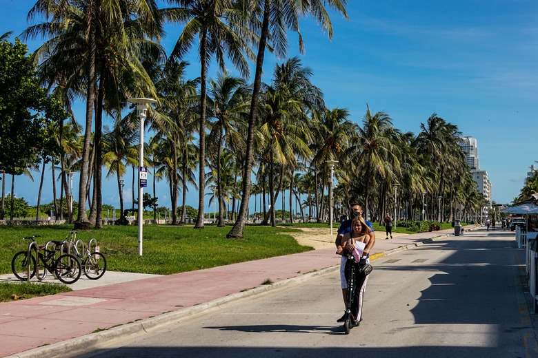 A couple rides an electric scooter on Ocean Drive in South Beach, Miami, on June 9, 2020. - Miami-Dade County beaches that were closed due to coronavirus pandemic will open on June 10, with visitors required to follow new social distancing guidelines. (Photo by CHANDAN KHANNA / AFP) (Photo by CHANDAN KHANNA/AFP via Getty Images)