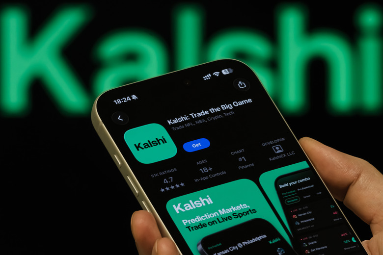 CHONGQING, CHINA - FEBRUARY 8: In this photo illustration, a person holds a smartphone displaying the Kalshi app page on the Apple App Store, with the Kalshi branding visible in the background, on February 8, 2026, in Chongqing, China. Kalshi, a U.S.-regulated prediction market platform that allows users to trade on the outcomes of real-world events, has surged in popularity and recently climbed to second place on the Apple App Store's U.S. free apps ranking, highlighting growing public interest in event-based financial markets and outcome forecasting. (Photo illustration by Cheng Xin/Getty Images)